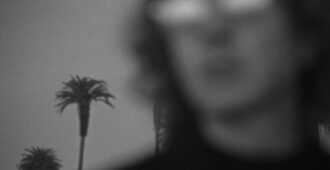 El músico estadounidense Beck difusamente con palmeras de fondo en el video musical de su canción Thinking About You del año 2023