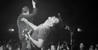 Imagen blanco y negro con integrantes de la banda inglesa de rock Blur tocando arriba de escenario en el video musical de su canción St. Charles Square que pertenece a su álbum de estudio The Ballad of Darren del año 2023
